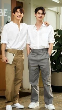 two young men standing next to each other wearing white shirts and khaki pants