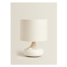 a white table lamp with a white shade on the base and a light bulb in the middle