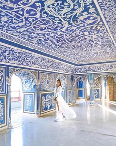 a woman in a white dress walking through a room with blue and white tiles on the ceiling