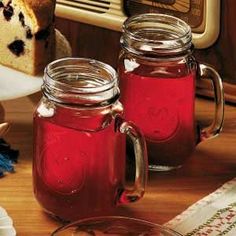 two jars filled with red liquid next to a slice of cake