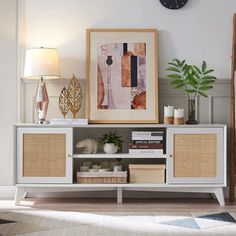 a white entertainment center with wicker baskets on the bottom shelf and a clock above it