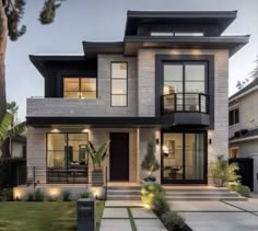 a large modern house with lots of windows and lights on the front door, surrounded by greenery