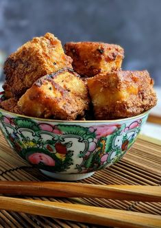 a bowl filled with fried food next to chopsticks on top of a table