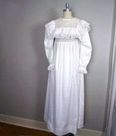 a white dress on a mannequin stand in front of a gray wall and wooden floor