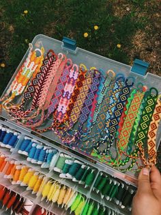 a person holding an open box filled with lots of different colored thread spools