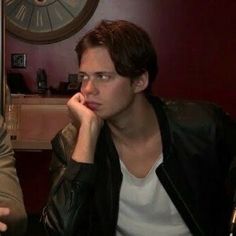 two young men sitting next to each other in front of a wall with a clock on it