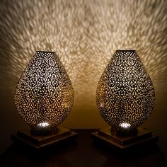 two vases sitting on top of wooden bases under a light that is reflecting off the wall