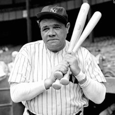 an old man holding two baseball bats in his hands while wearing a new york yankees uniform