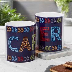 two coffee mugs sitting on top of a table next to cookies and crackers