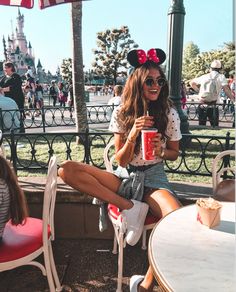 a woman sitting at a table with a drink in her hand and minnie mouse ears on her head