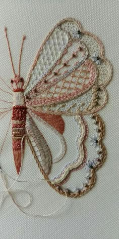 a close up of a butterfly on a piece of white fabric with red and orange thread