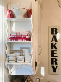 a white cabinet filled with dishes and plates next to a sign that says bakery