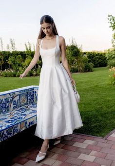 a woman in a white dress standing next to a blue and white bench on grass