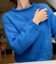 a woman in a blue sweater is holding her hand on her chest and looking at the camera