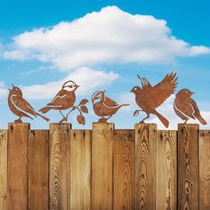 five metal birds sitting on top of a wooden fence