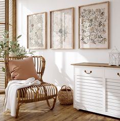 a room with white walls and wooden flooring, two framed pictures on the wall next to a wicker chair