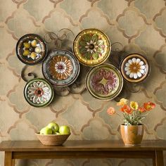 there are many plates on the wall with flowers and fruit in bowls next to them