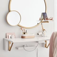 a white desk with a round mirror on the wall above it and other items in front of it