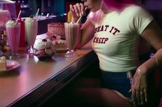 a woman sitting at a table with several drinks and desserts on the counter in front of her