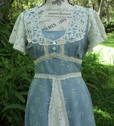 "Today I have a Vintage, Gunne Sax dress of a muted, Fall blue (medium weight cotton) with cream-colored posies and heavy lace adornments. The silhouette is an Aline and the waist is in the high, empire style. The bodice is adorned with heavy, floral lace that is tightly woven to produce a sheen and 3 buttons are in place vertically for interest below a privacy panel. Heavy weight, floral lace comprises the flutter sleeves and is also present on the apron. As stated above, the waist is high and Vintage Gunne Sax Dress, Fall Blue, Sax Dress, Gunne Sax Dress, Muted Blue, Gunne Sax, Empire Style, Dress With Tie, Flutter Sleeves