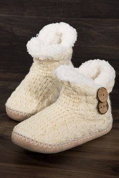 a pair of knitted slippers with buttons on the front and bottom, sitting on a wooden floor