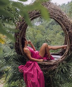 a woman in a pink dress laying on top of a tree with a bird nest