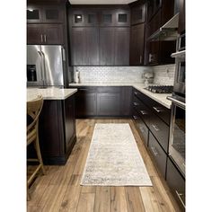 a kitchen with dark wood cabinets and white rugs on the hardwood floor, along with stainless steel appliances