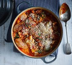 a pot filled with meat and vegetables on top of a wooden table next to a spoon