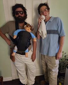 two men standing next to each other with one holding a doll and the other wearing sunglasses