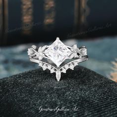 a princess cut diamond engagement ring on top of a black velvet cushioned surface with books in the background