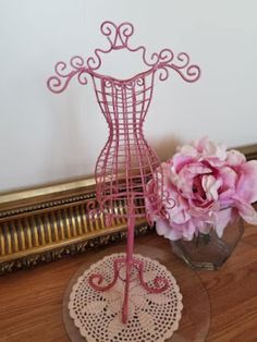 a pink flower in a vase next to a wire mannequin on a table