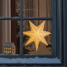 a yellow paper star hanging from a window sill in front of a snowy scene