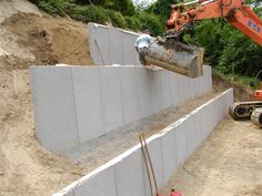 an excavator is working on the construction of a retaining wall with concrete blocks