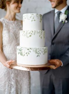 a bride and groom holding a wedding cake on a wooden platter in front of them