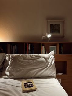 a book is laying on top of a bed with white sheets and pillows, in front of a bookshelf