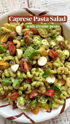 a white bowl filled with pasta salad and topped with pesto, cherry tomatoes and mozzarella