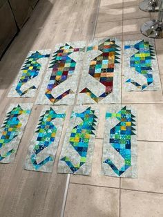 four quilts laid out on the floor to be made into wall hangings with blue and green designs