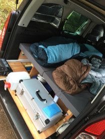 an open car trunk with clothes and other items in the cargo area, including sleeping bags