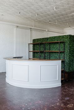 a white reception table with green plants on the back wall and shelves in front of it