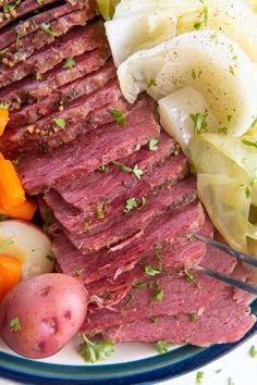 corned beef, potatoes and carrots on a blue and white plate with a fork