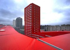 a red building is seen from the top of a tall building, with other buildings in the background