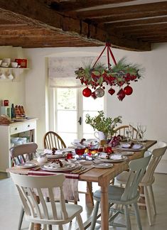 a dining room table set for christmas with ornaments hanging from the ceiling and plates on it