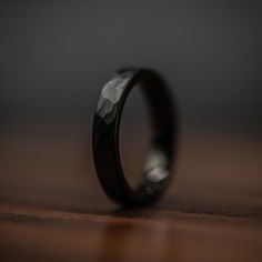 a wedding band with black diamond inlays sits on a wooden table, ready to be used as a ring