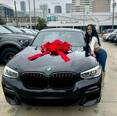 a woman standing next to a black car with a red bow on it