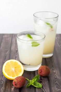 two glasses filled with lemonade sitting on top of a wooden table next to strawberries