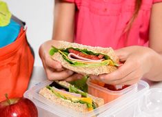 a person holding a sandwich in their hands with an apple and water bottle behind them