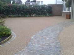 an empty driveway in front of a house with bushes and shrubs on either side of it