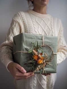 a woman is holding a wrapped present with dried flowers and leaves on it in her hands