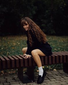 a woman is sitting on a bench in the park and smiling at the camera with her legs crossed