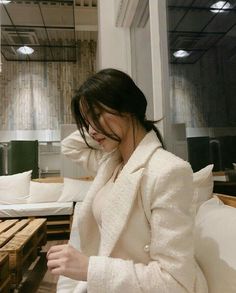 a woman sitting on top of a white couch next to a wooden table with a cell phone in her hand